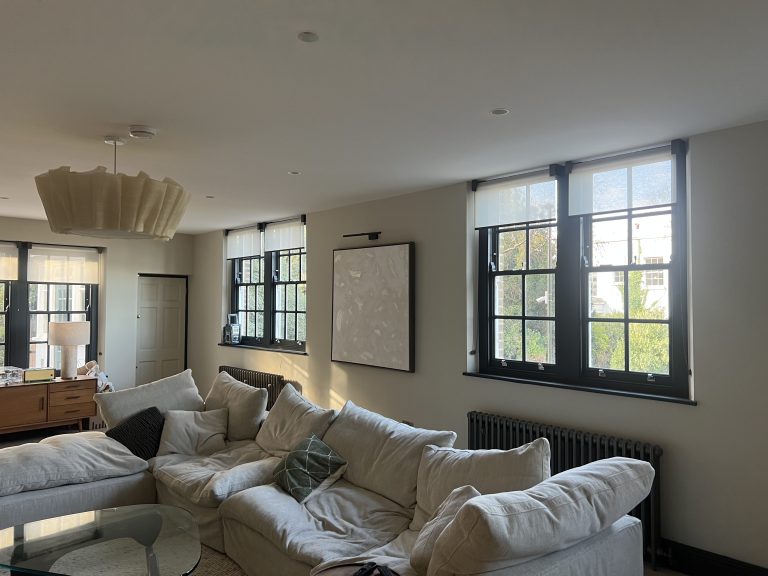 Lewis Capaldy – Bright living room with large, black-framed windows a cream sectional sofa with cushions wall art and a modern pendant light